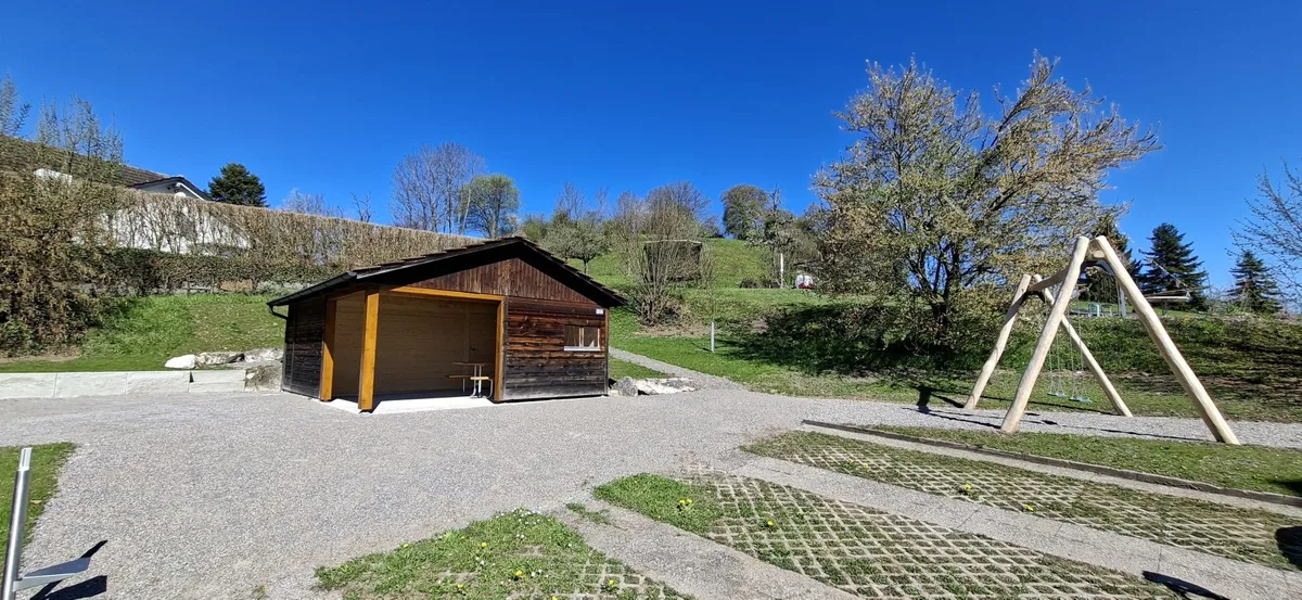 Der neue Spielplatz in Ottikon: Man sieht eine Holzhütte mit Laube und eine Kinderschaukel.